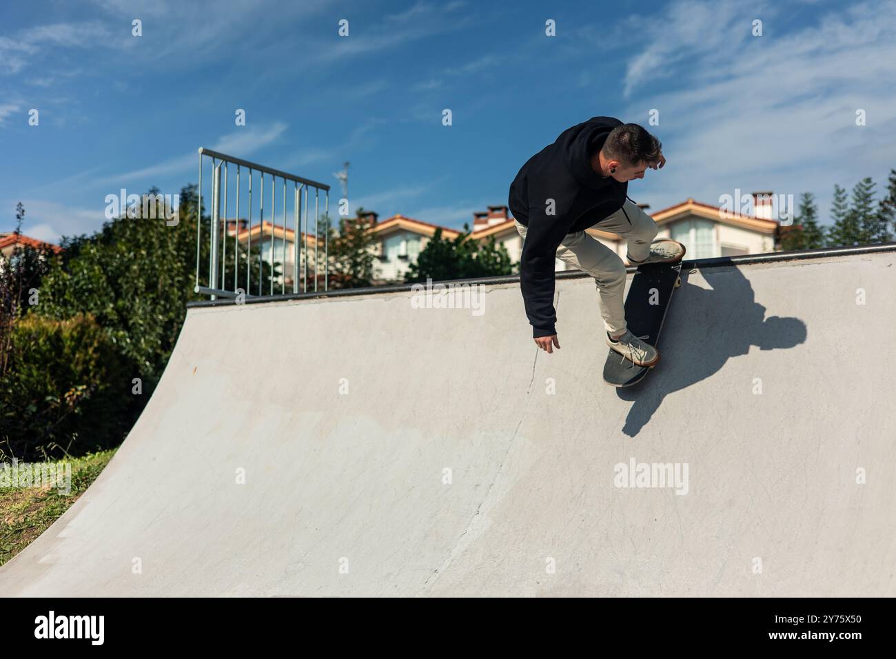 patineur à mi-parcours, descendant le half-pipe à un skate park sous le ciel clair et ensoleillé. la scène extérieure capture l'essence du skateboard, avec le Banque D'Images