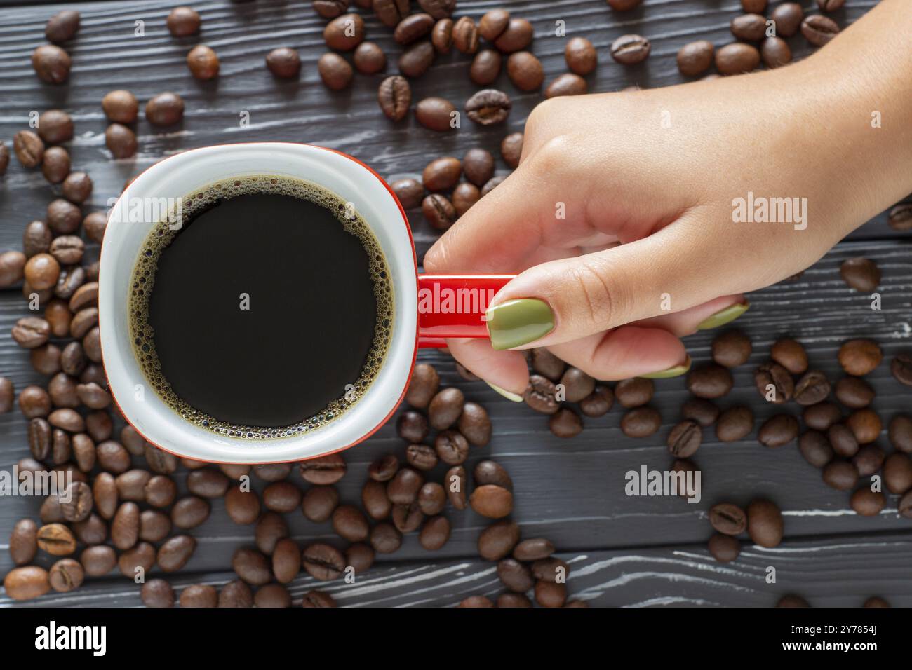 Main féminine tenant une tasse de café sur un fond de grains de café couché sur la table, vue de dessus Banque D'Images