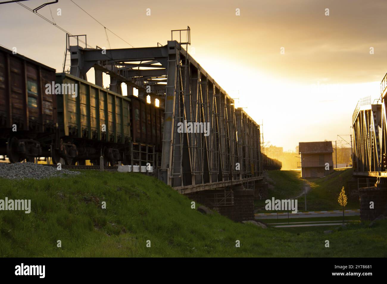 Mise au point sélective.Wagons de marchandises sur un pont ferroviaire tirés par un train.Lumière du soleil du soir et reflet de la lumière orange du soir de la structure métallique Banque D'Images