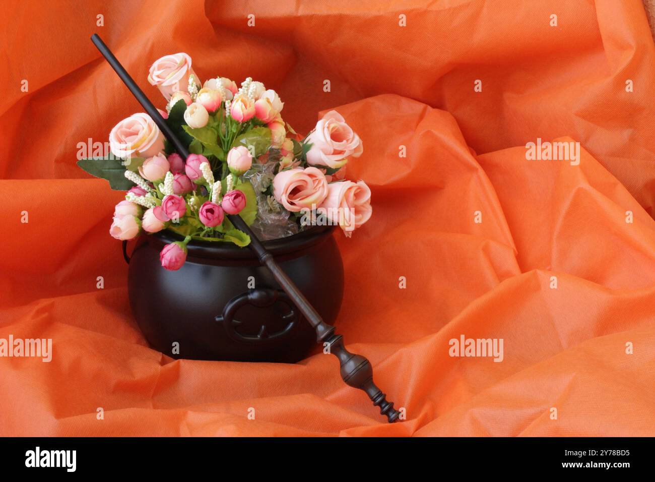 Baguette magique sur des boutons de rose à l'intérieur d'un chaudron de sorcière. Décoration d'Halloween sur fond de couleur orange. Jour de la célébration des morts. Espace de copie disponible. Banque D'Images