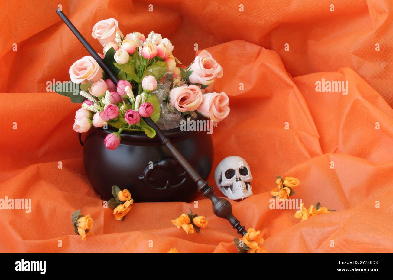 Baguette magique sur des boutons de rose à l'intérieur d'un chaudron de sorcière. Crâne effrayant et fleurs sur fond de couleur orange pour la célébration d'Halloween. Le jour du décor des morts. Banque D'Images