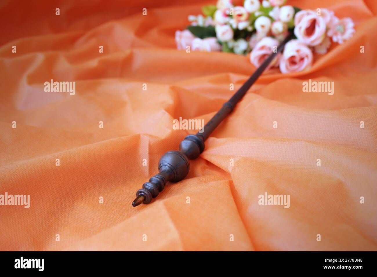 Baguette magique de sorcière sur fond de tissu de couleur orange avec roses roses délicates romantiques. Espace de copie disponible. Banque D'Images