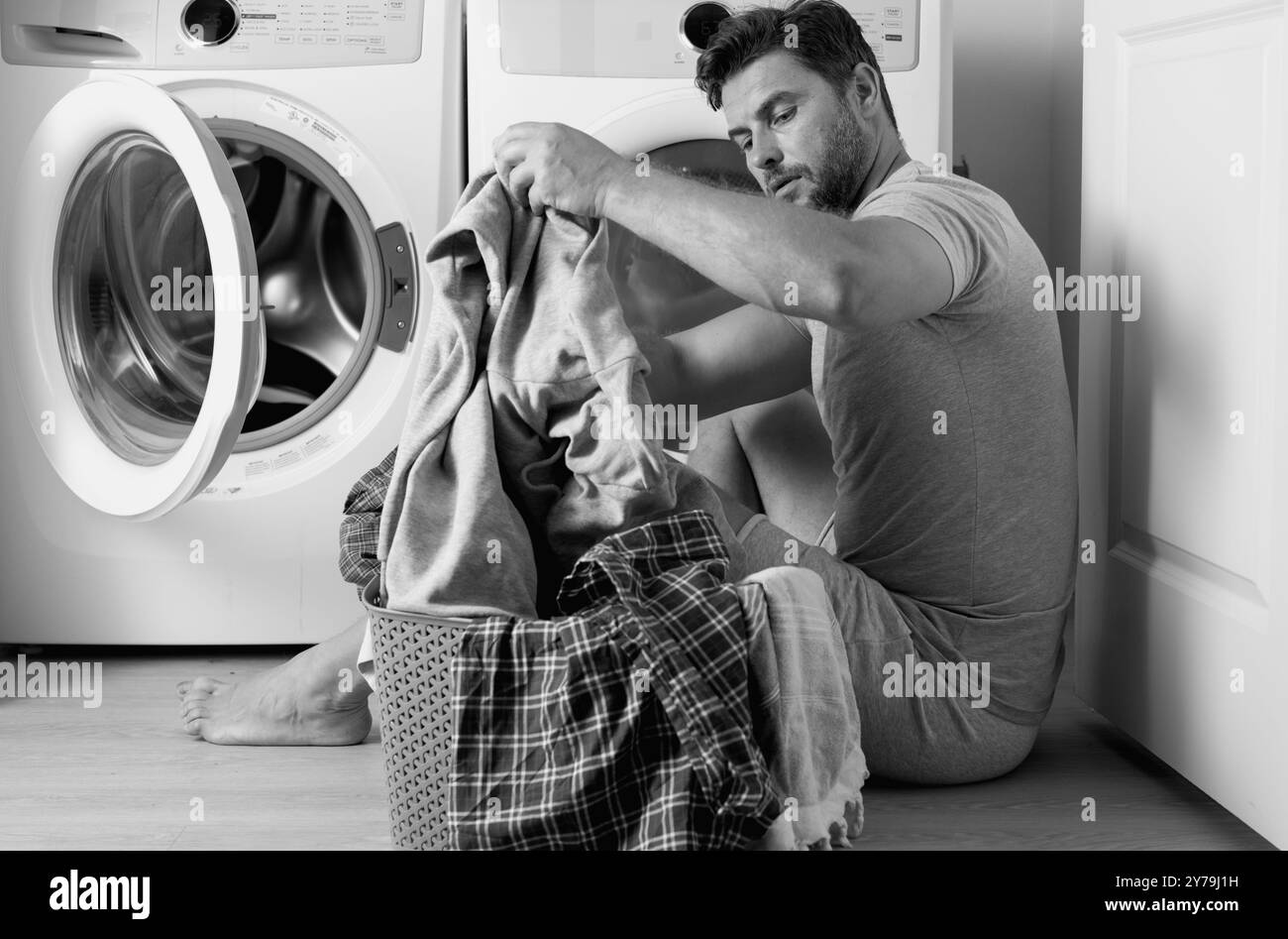 Homme chargeant les vêtements dans la machine à laver dans la buanderie. Homme d'âge moyen mettant le linge dans la machine à laver peur et stupéfait avec la bouche ouverte pour Banque D'Images