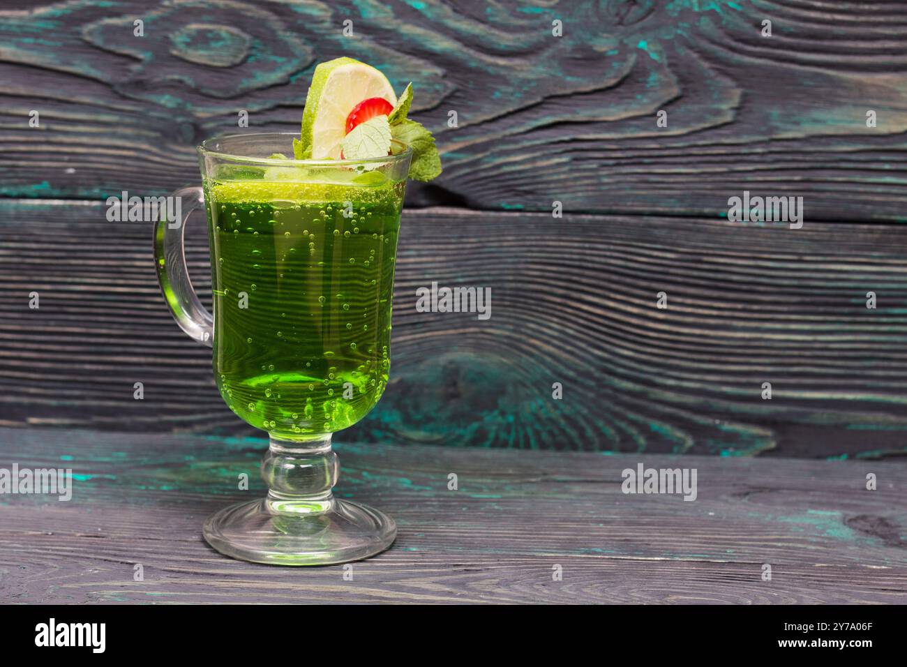 Limonade verte dans un verre. Décoré de citron vert et de fraises. Avec des brins de menthe. Sur des planches de pin. Banque D'Images