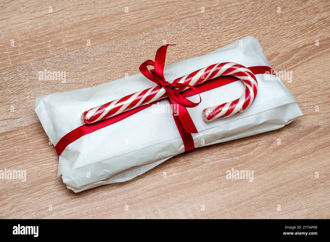 Cadeau de Noël enveloppé avec du papier blanc et un ruban rouge, décoré de cannes de bonbons. Banque D'Images