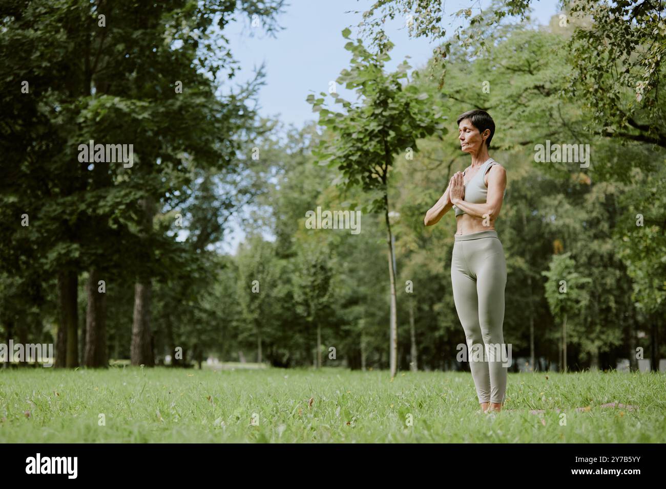Femme caucasienne senior médiatrice dans un parc verdoyant, elle se tenait immobile sur une pelouse verte et immergée dans les pensées Banque D'Images