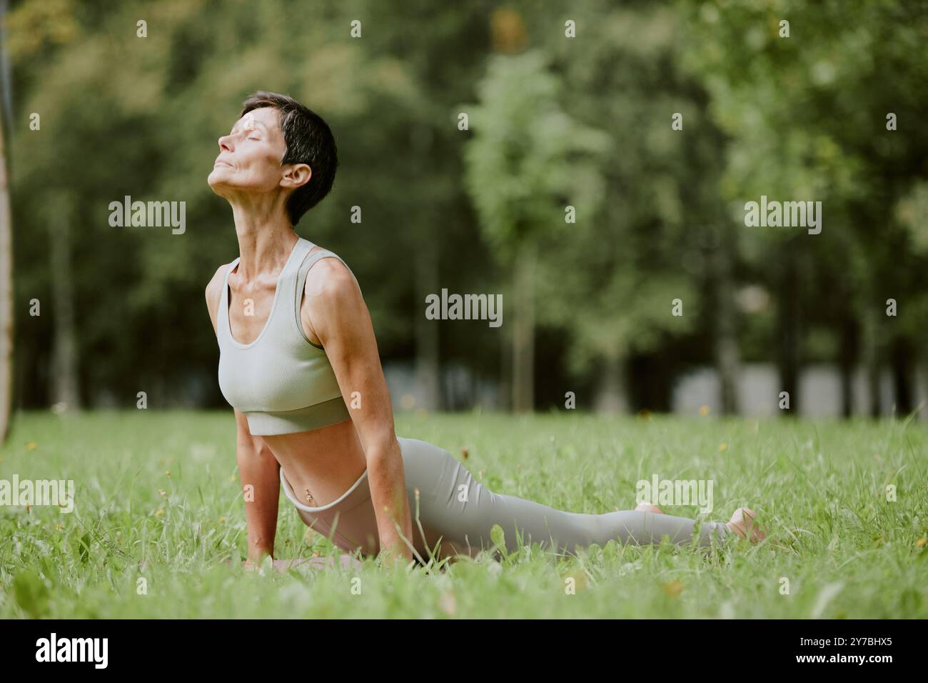 Femme senior immergée dans les pensées tout en se tenant debout dans la position Urdhva Mukha Svanasana sur la pelouse fraîche coupée Banque D'Images