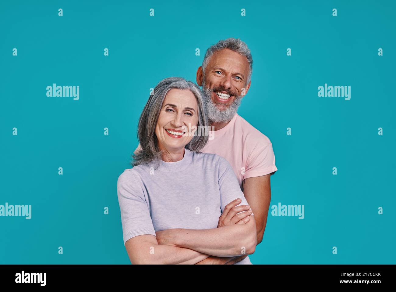 Beau couple senior regardant la caméra et souriant tout en se tenant debout ensemble sur fond bleu Banque D'Images
