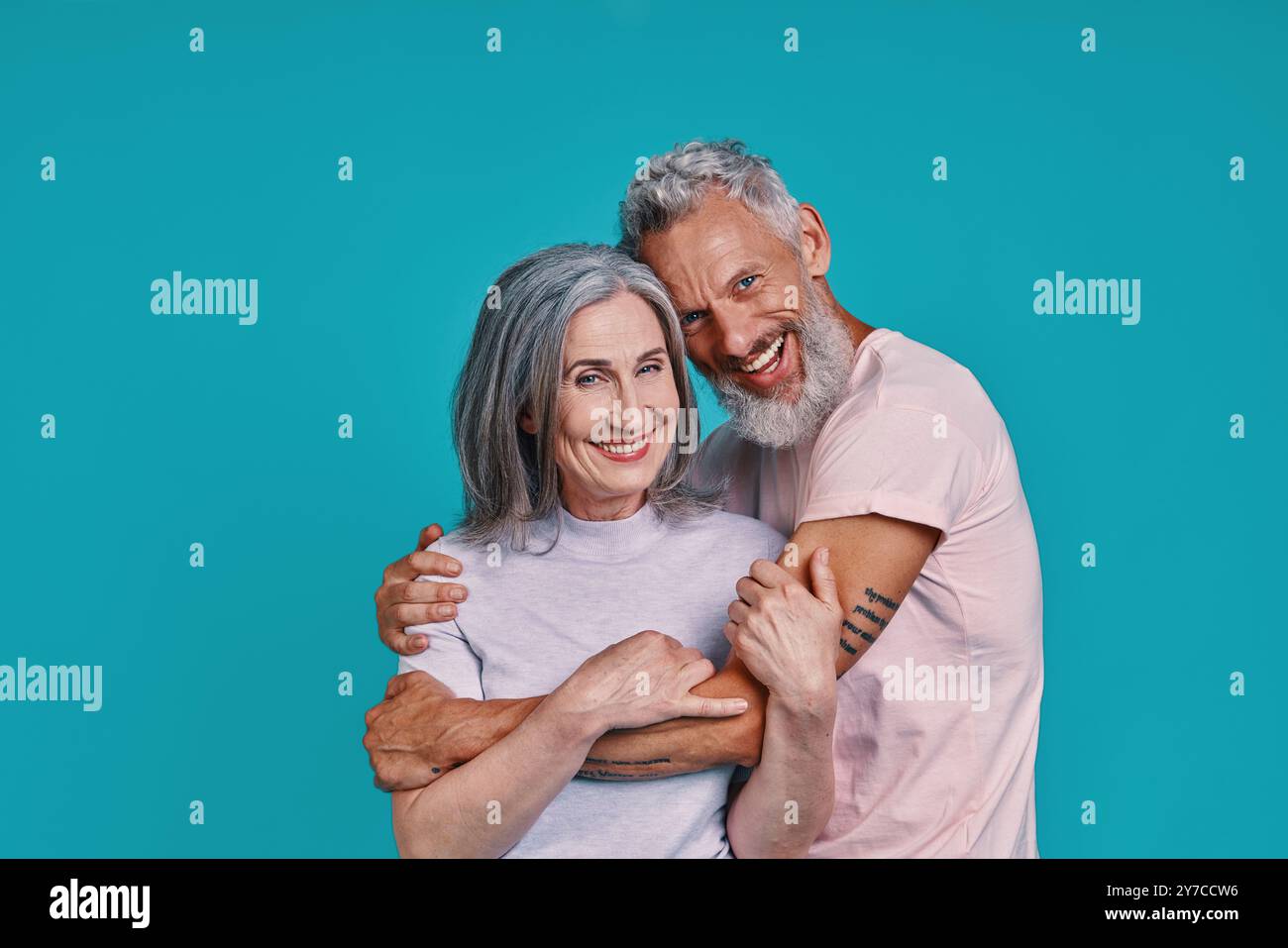Couple senior romantique regardant la caméra et souriant tout en se tenant debout ensemble sur fond bleu Banque D'Images