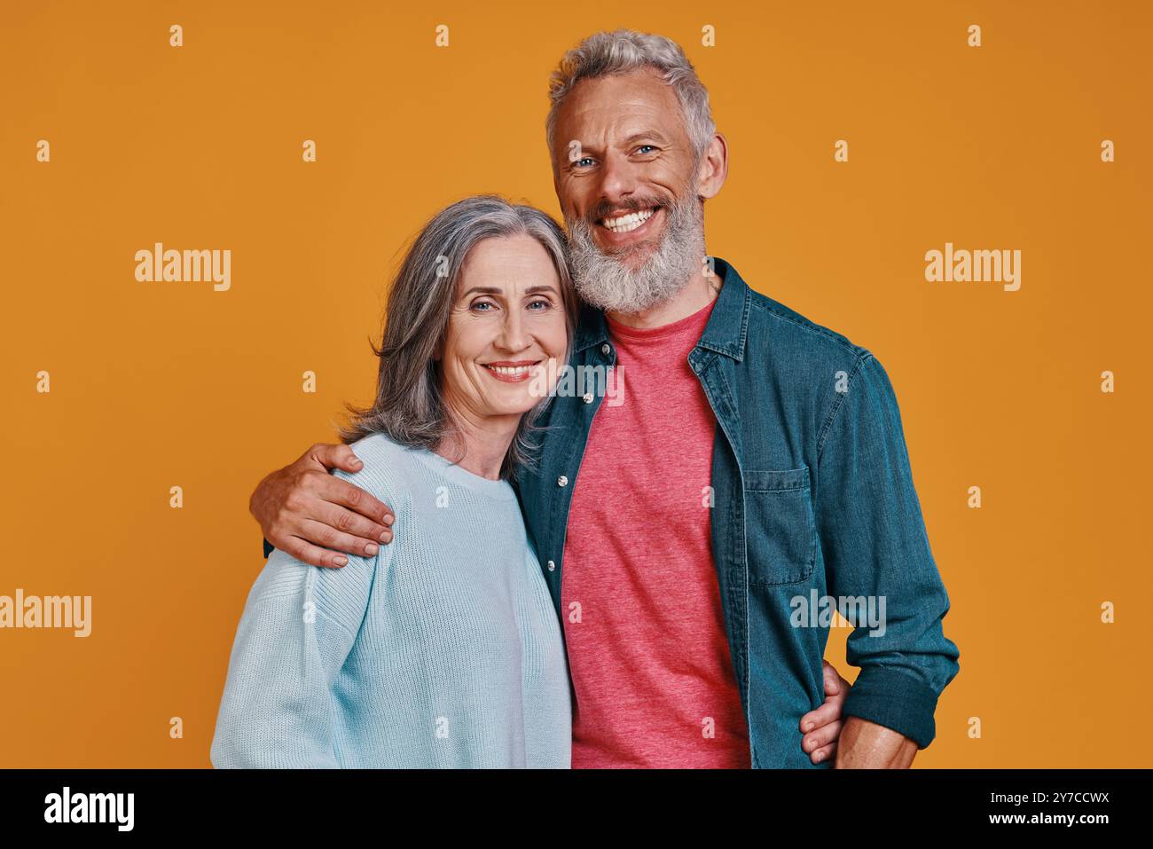 Couple senior romantique regardant la caméra et souriant tout en se tenant debout ensemble sur fond orange Banque D'Images