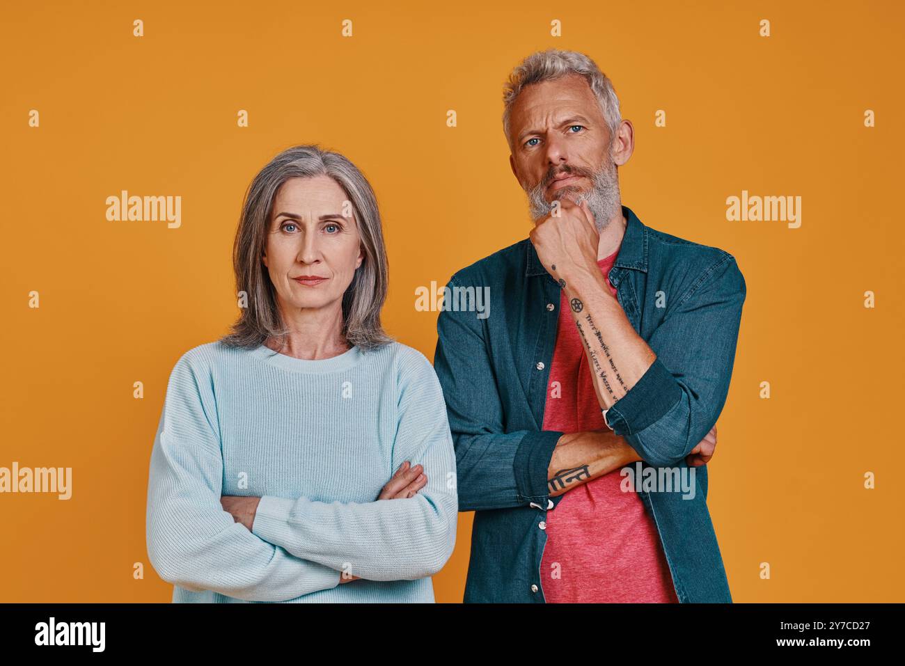 Couple aîné réfléchi regardant la caméra tout en se tenant debout ensemble sur fond orange Banque D'Images