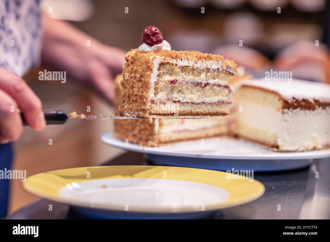 Stück Frankfurter Kranz wird serviert 25.09.24, Limbourg : Symbolfoto, Illustrationsbild, Symbolbild, Illustrationsfoto, Alltagsszene Stück Frankfurter Kranz wird serviert eine person serviert ein Stück Frankfurter Kranz auf einem gelben Teller. Der klassische deutsche Kuchen ist in Schichten aufgebaut, mit Buttercreme und Johannisbeermarmelade gefüllt und mit Krokant sowie einer Kirsche dekoriert. Limburg Hessen Allemagne *** morceau de Frankfurter Kranz servi 25 09 24, Limburg Symbol photo, illustration image, symbole image, illustration photo, illustration photo, pièce de scène quotidienne de Frankfurter Kranz BEI Banque D'Images