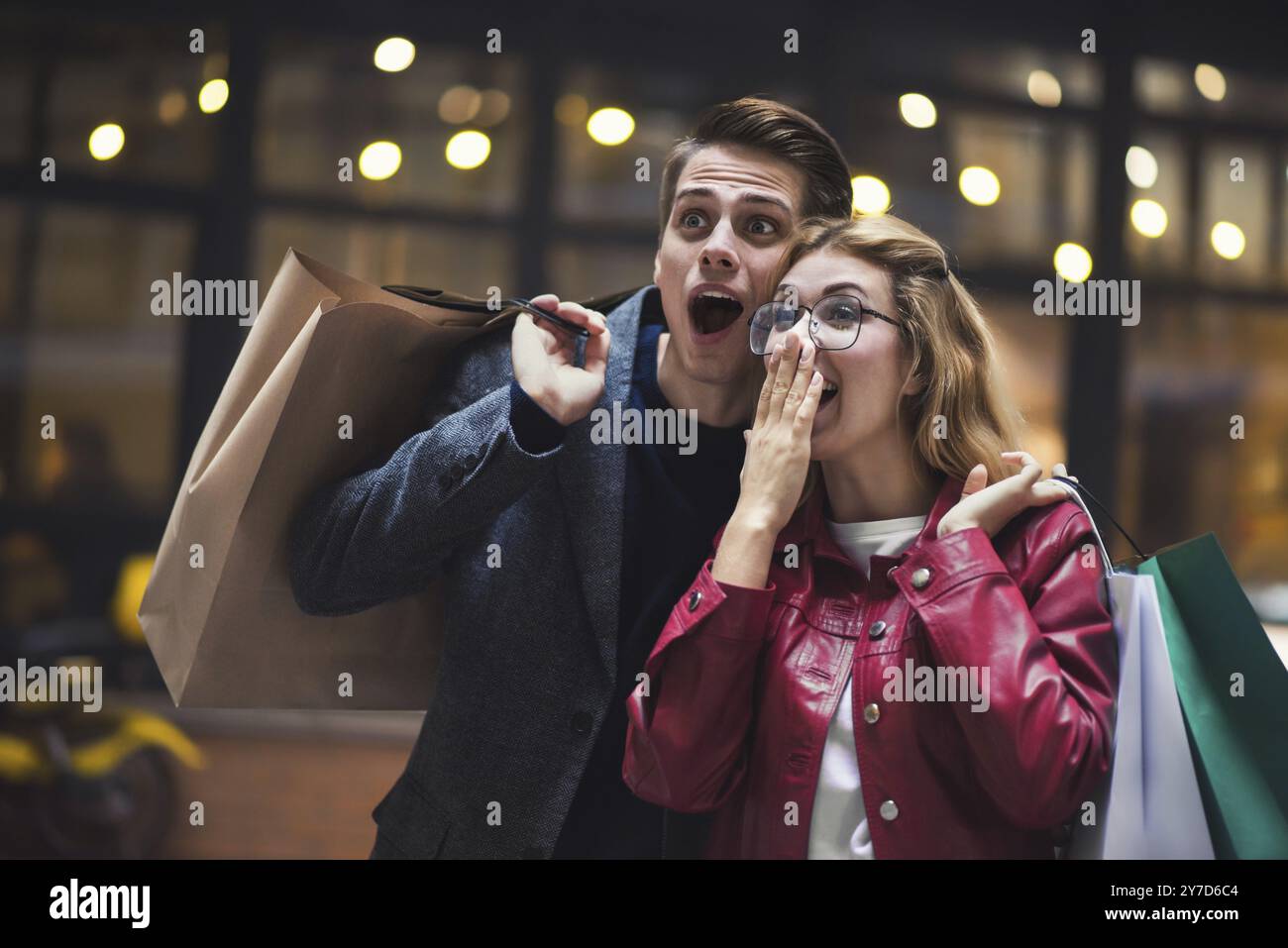 Beau couple avec des sacs à provisions parle et sourit tout en faisant du shopping dans le centre commercial se concentrer sur la femme surprise Banque D'Images