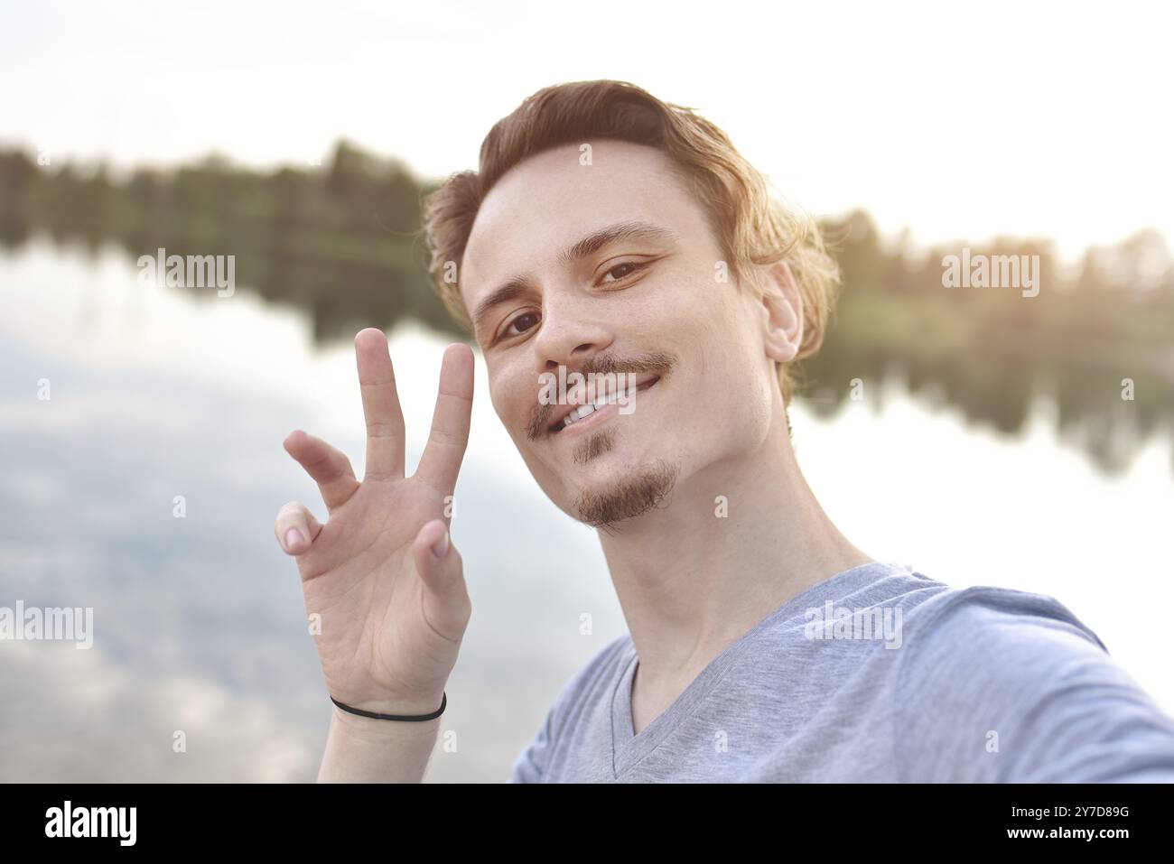 Portrait de jeune beau gars élégant souriant fait selfie contre le lac. belle nature Banque D'Images