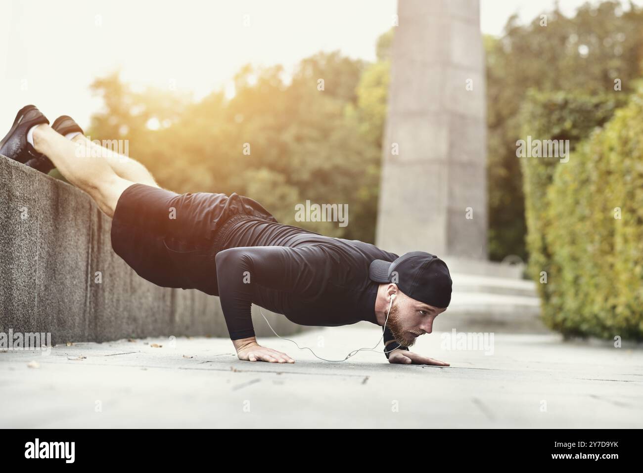 Jeune sportif barbu fait de l'entraînement dans un parc, faisant une série de pompes en plein air Banque D'Images