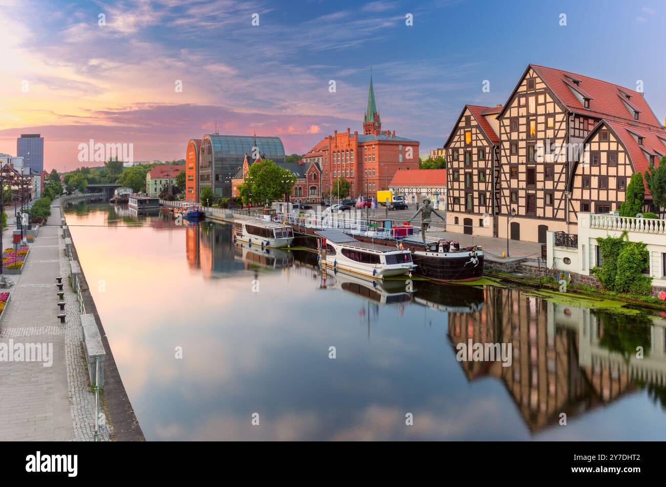 Vue panoramique sur le front de mer de Bydgoszcz au lever du soleil avec des bateaux le long de la rivière Brda, des bâtiments historiques à colombages et des structures modernes en Pologne Banque D'Images