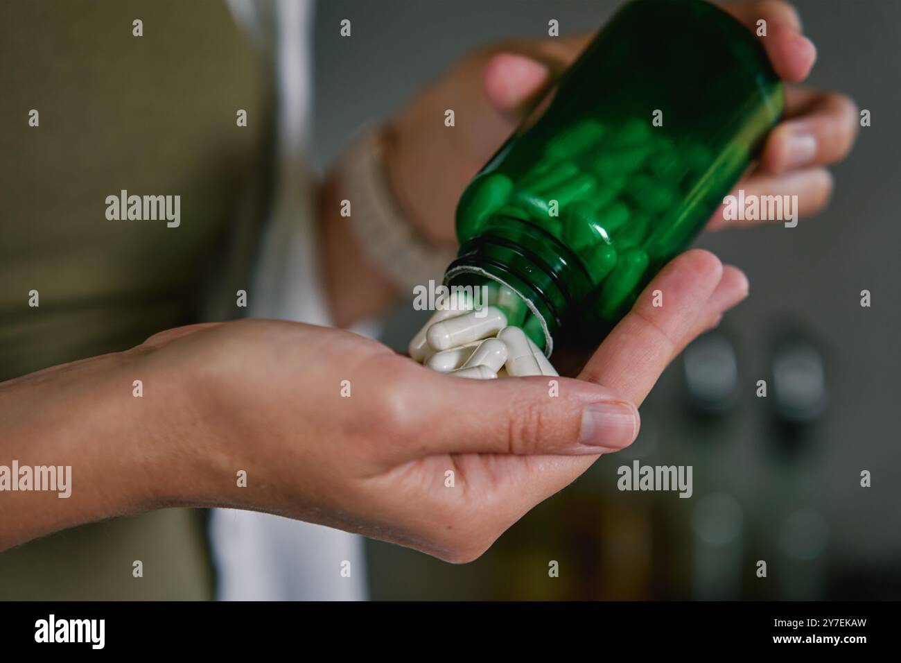 Gros plan de la femme versant des capsules blanches de la bouteille verte dans la main. La personne prend des pilules ou des vitamines. Concept de suppléments, de médicaments ou de santé c Banque D'Images