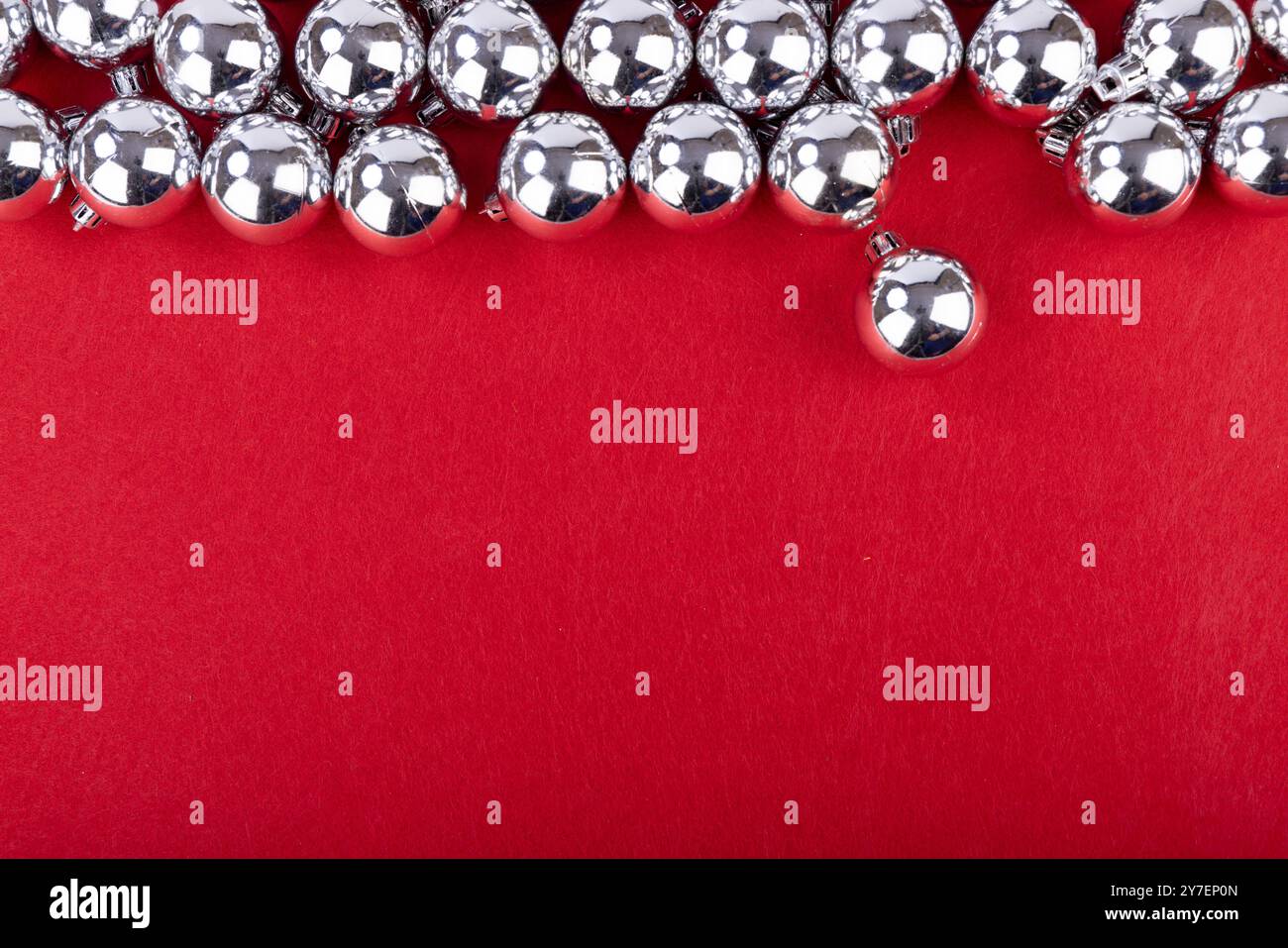 Un arrangement festif de boules de Noël argentées reposant sur un fond rouge vif, créant une atmosphère de vacances joyeuse Banque D'Images