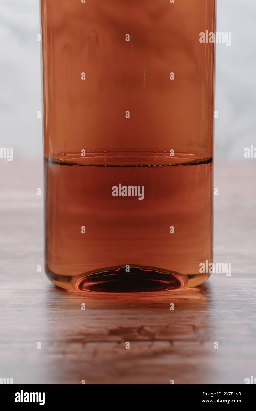 Une bouteille semi-transparente marron avec du liquide sur une table en bois, placée sur un fond lumineux et minimaliste. Banque D'Images