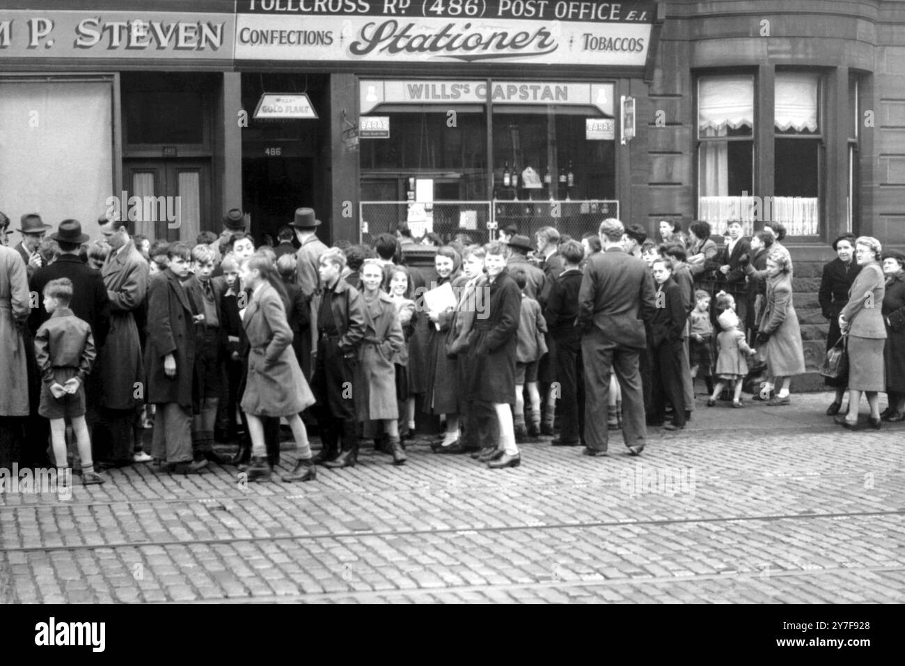 Glasgow : une petite foule se rassemble autour d'un bureau de poste secondaire à Tollcross Road, Glasgow, après qu'un bandit armé s'est échappé du magasin. blesser le maître de poste à la jambe. En courant dans la rue, le tireur a attrapé une femme au foyer de 65 ans, Mme Cathrine Fleming, et l'a utilisée comme un mouillage alors que la police s'approchait. Puis il a paniqué, l'a laissée partir, et saisi par la police, a été embarqué dans une voiture. Deux hommes auraient été impliqués dans le hold-up et l'argent volé au bureau de poste n'a pas été récupéré. L'homme arrêté a ensuite été inculpé d'un certain nombre de chefs d'accusation. 2 octobre 1952 Banque D'Images