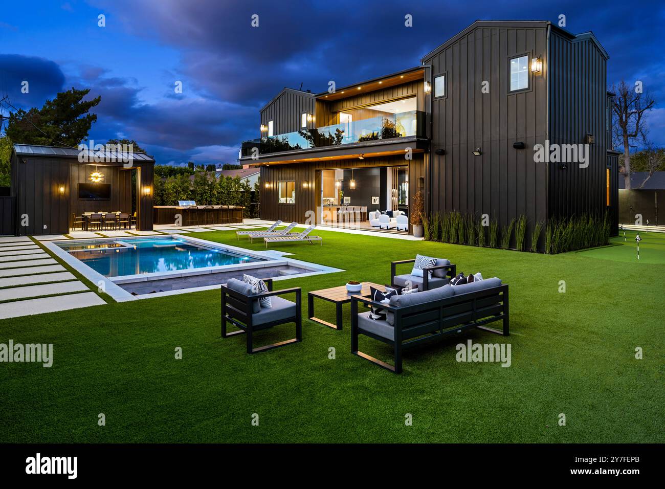 Maison de luxe moderne avec piscine, sièges extérieurs et pelouse bien entretenue au crépuscule. Banque D'Images