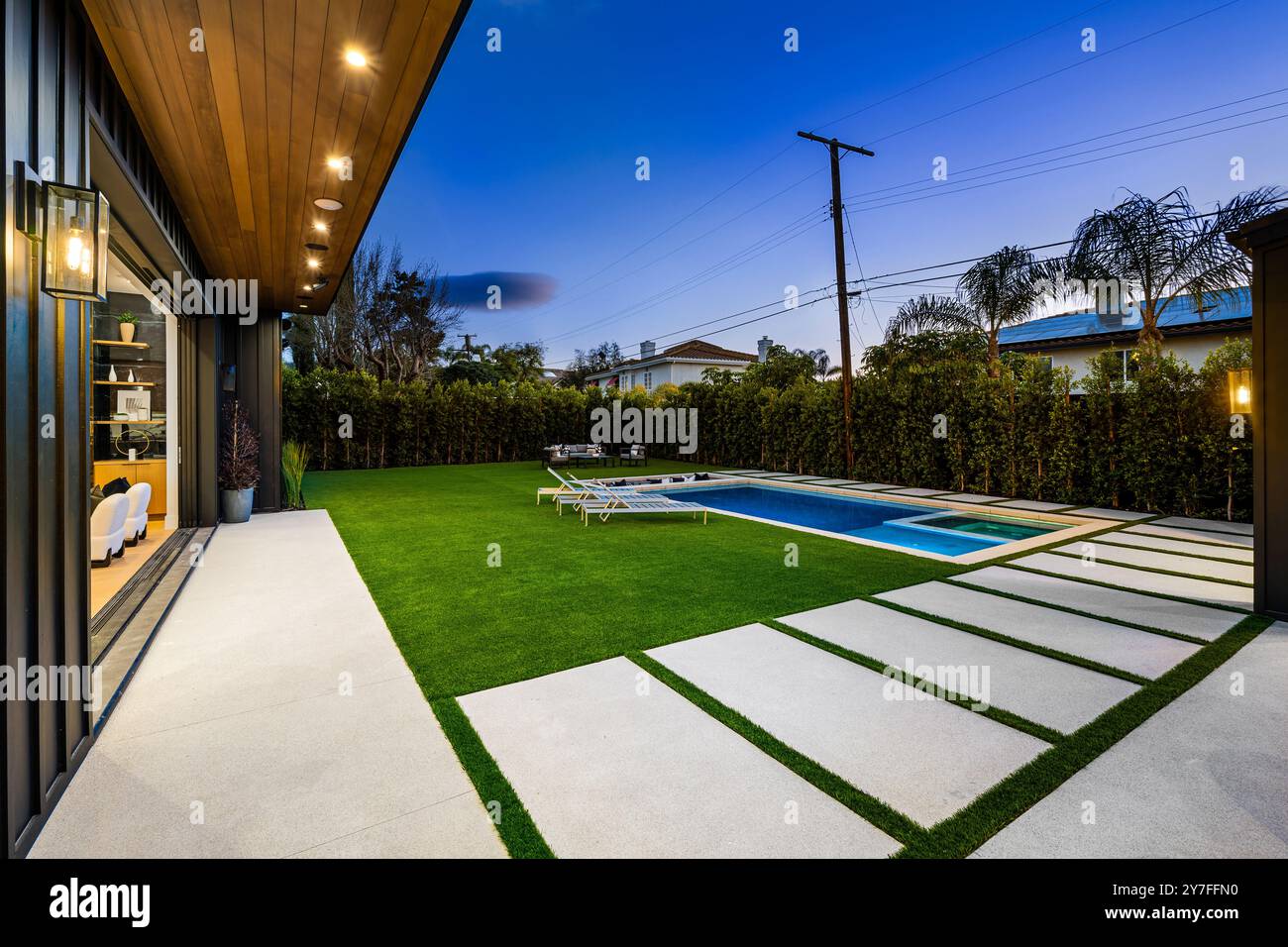 Jardin moderne avec piscine et pelouse bien entretenue au crépuscule, avec mobilier d'extérieur contemporain et éclairage d'ambiance. Banque D'Images