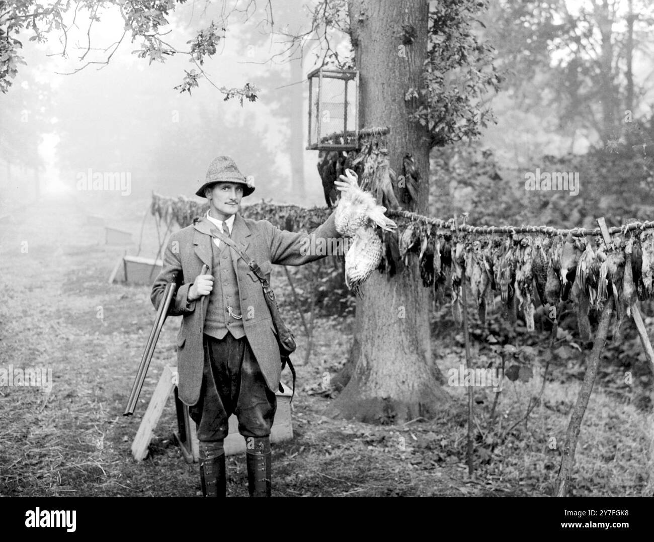 Un gardien de pays, vêtu de culottes et de guêtres en cuir avec son gibbet. Ces démonstrations macabres de vermine détruite et de prédateurs étaient autrefois un spectacle commun. Derrière le gardien peut être vu ses poulaillers pour l'élevage du faisan Banque D'Images