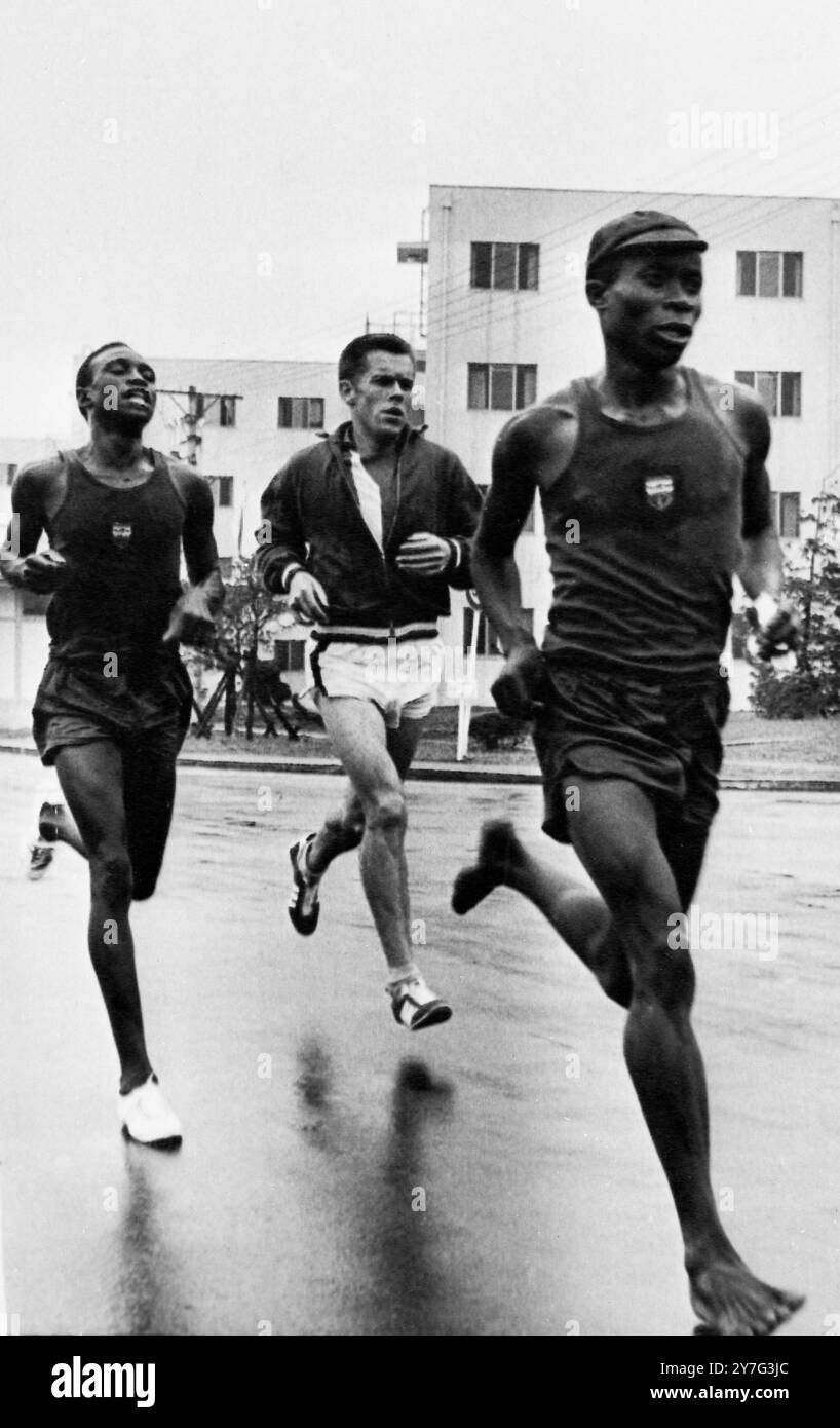 Entraînement pieds nus pour le marathon courir pieds nus comme il l'était lorsqu'il a remporté le marathon de Rome il y a quatre ans, l'éthiopien Bikila Abebe (à gauche) s'entraîne ici avec deux coureurs non identifiés au village olympique. 9 octobre 1964 Banque D'Images
