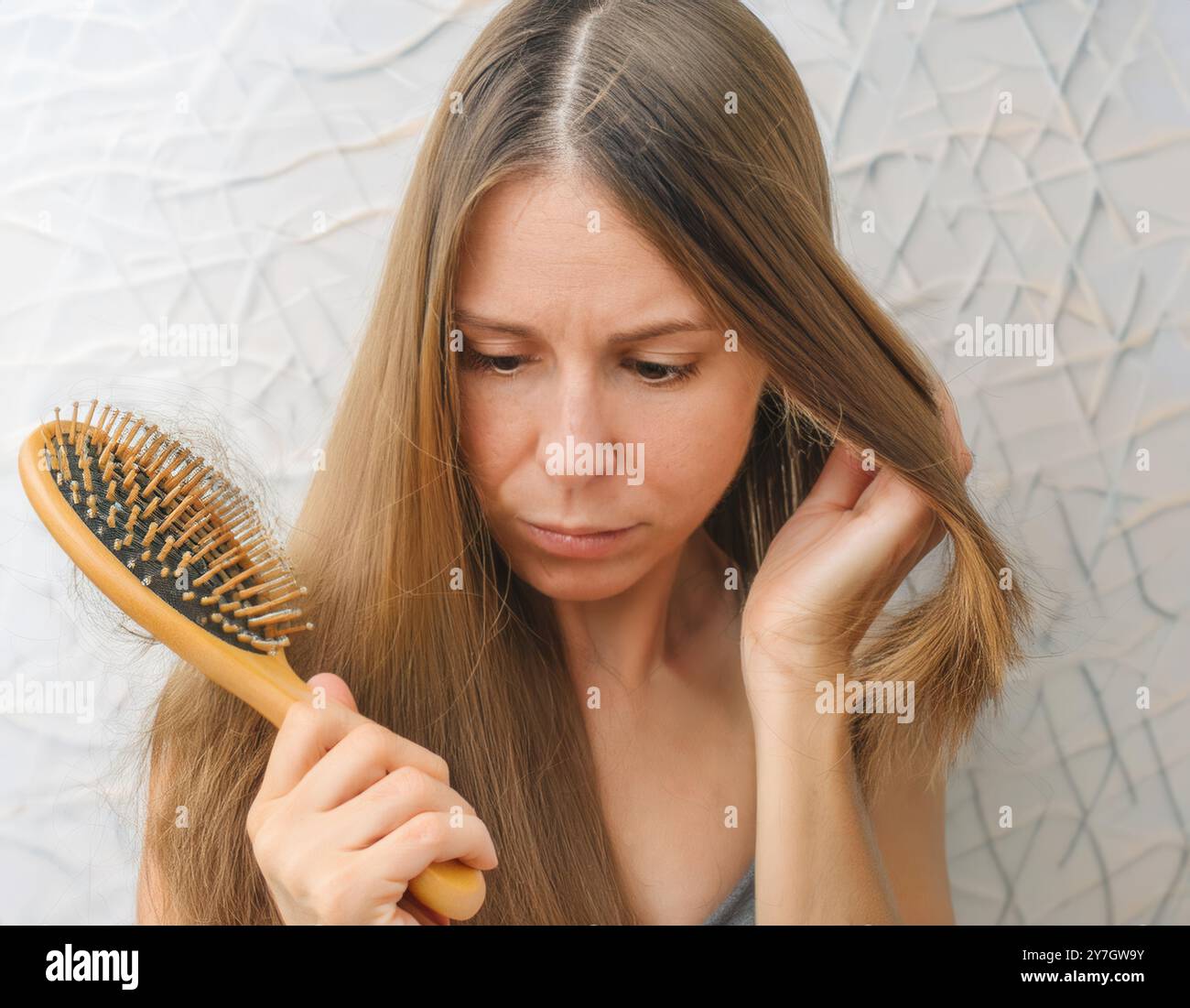 Une jeune femme se peigne les cheveux avec une brosse. De nombreux poils tombés pendant le peignage restent sur la brosse. Problèmes hormonaux ou manque de suppléments. Banque D'Images