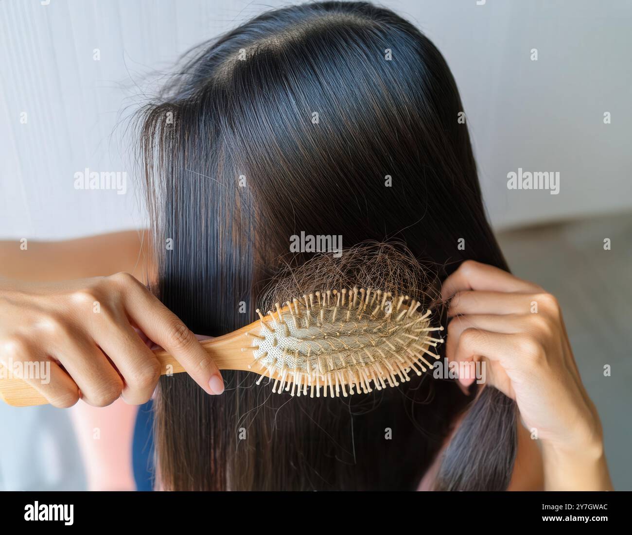 Une jeune femme se peigne les cheveux avec une brosse. De nombreux poils tombés pendant le peignage restent sur la brosse. Problèmes hormonaux ou manque de suppléments. Banque D'Images