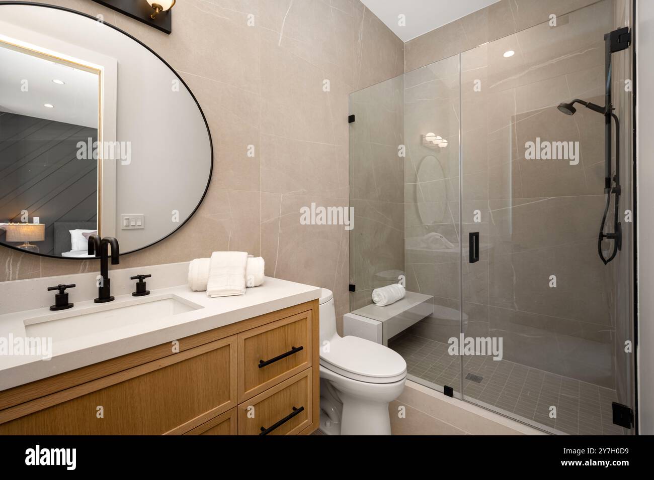 Salle de bains moderne avec cabine de douche en verre, meuble-lavabo en bois et grand miroir ovale aux tons neutres et aux luminaires contemporains. Banque D'Images