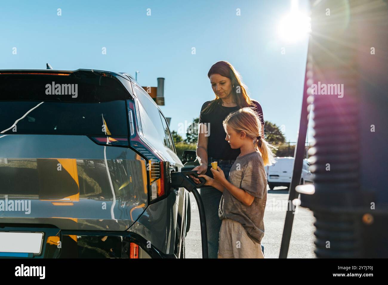 Mère apprenant son fils à charger la voiture tout en se tenant debout à la station de charge du véhicule Banque D'Images
