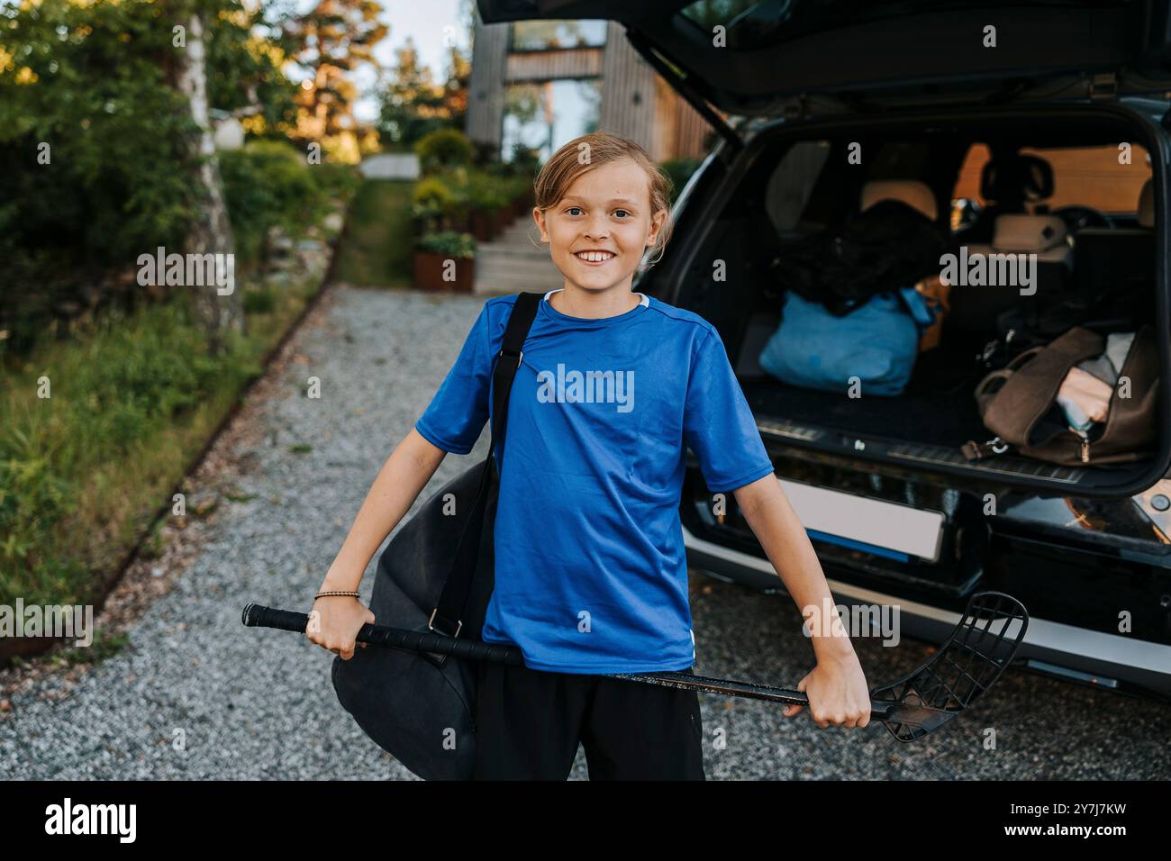 Portrait d'un garçon souriant tenant un bâton de hockey sur glace tout en se tenant devant le coffre de la voiture Banque D'Images