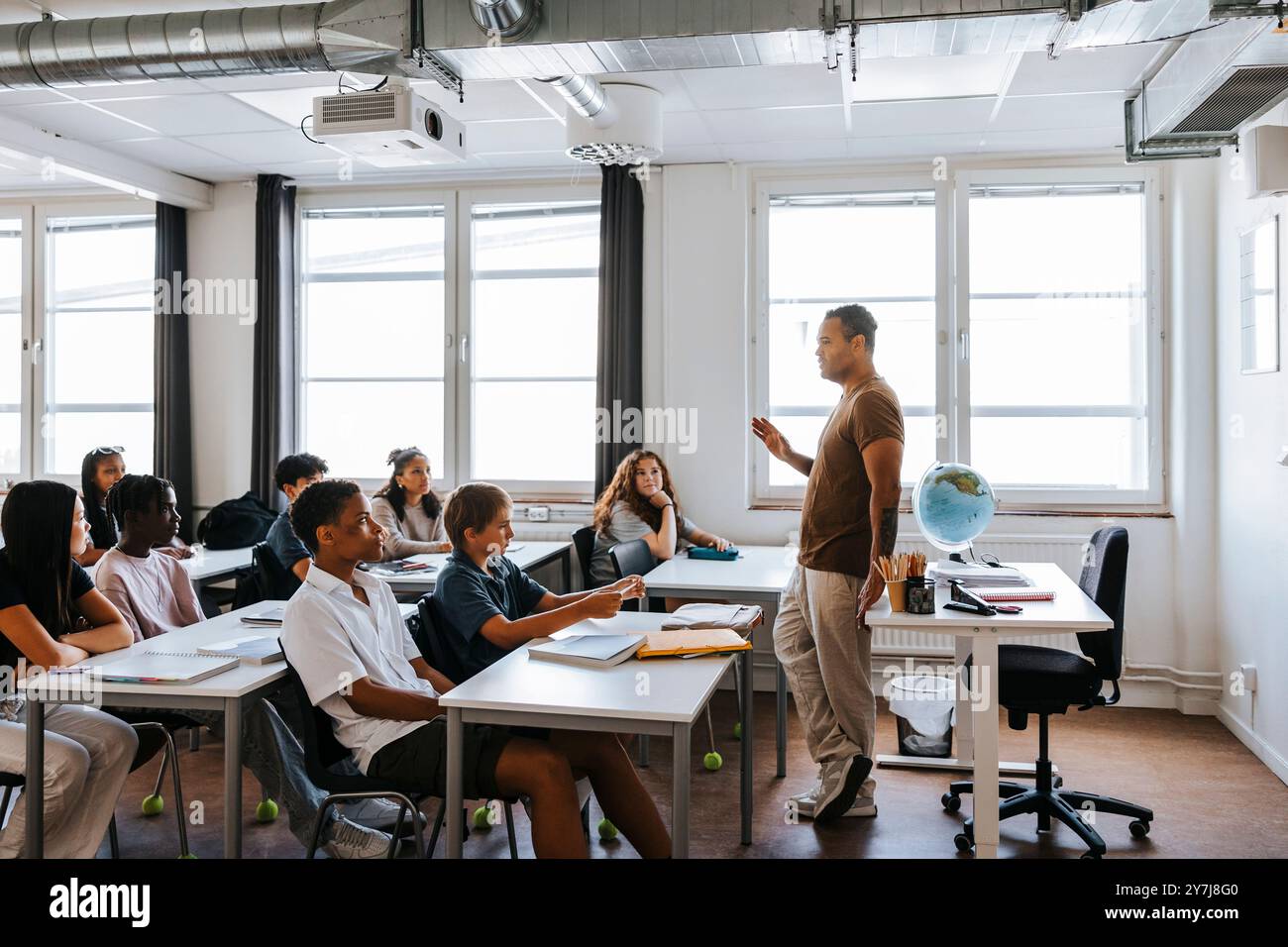 Enseignant masculin groupe d'élèves du premier cycle du secondaire assis en classe à l'école Banque D'Images