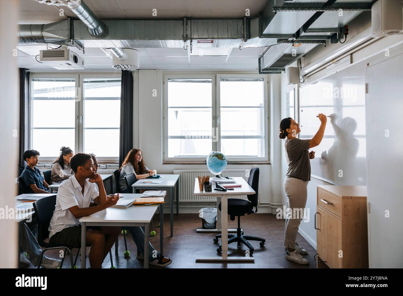 Professeur féminin écrivant sur le tableau blanc tout en enseignant des élèves du premier cycle du secondaire en classe à l'école Banque D'Images