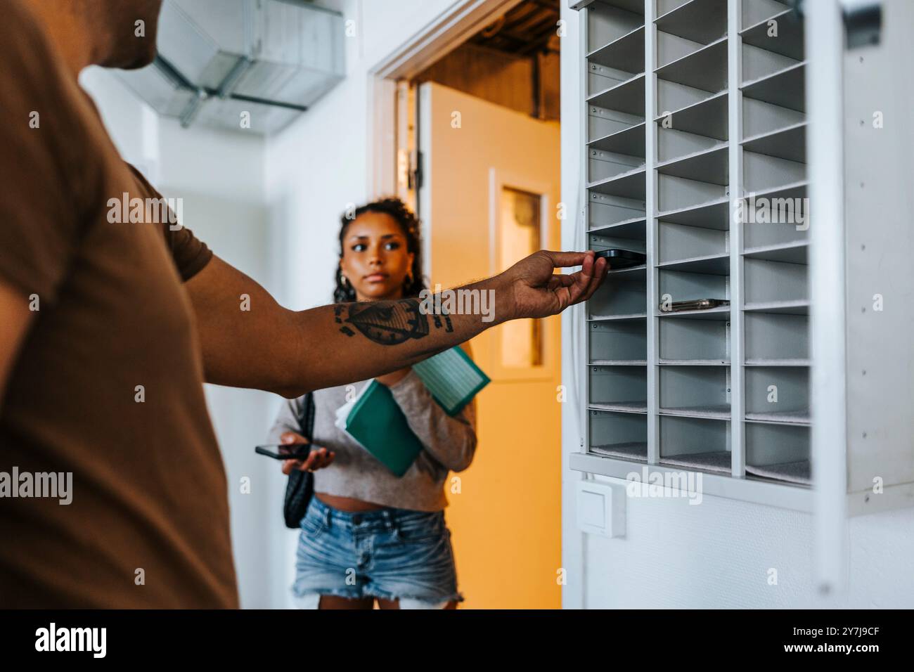 Milieu de section d'un enseignant masculin soumettant un téléphone intelligent dans un casier à l'école Banque D'Images