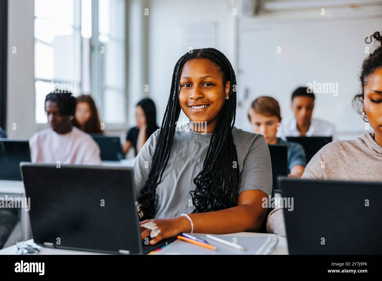 Portrait d'un adolescent avec des cheveux tressés assis avec un ordinateur portable en classe au collège Banque D'Images