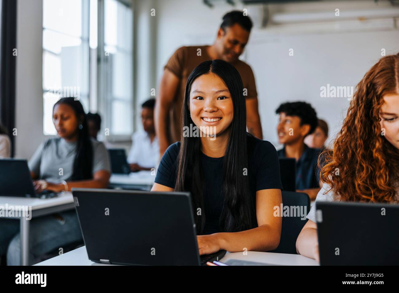 Portrait d'un adolescent souriant assis avec un ordinateur portable dans une salle de classe au collège Banque D'Images