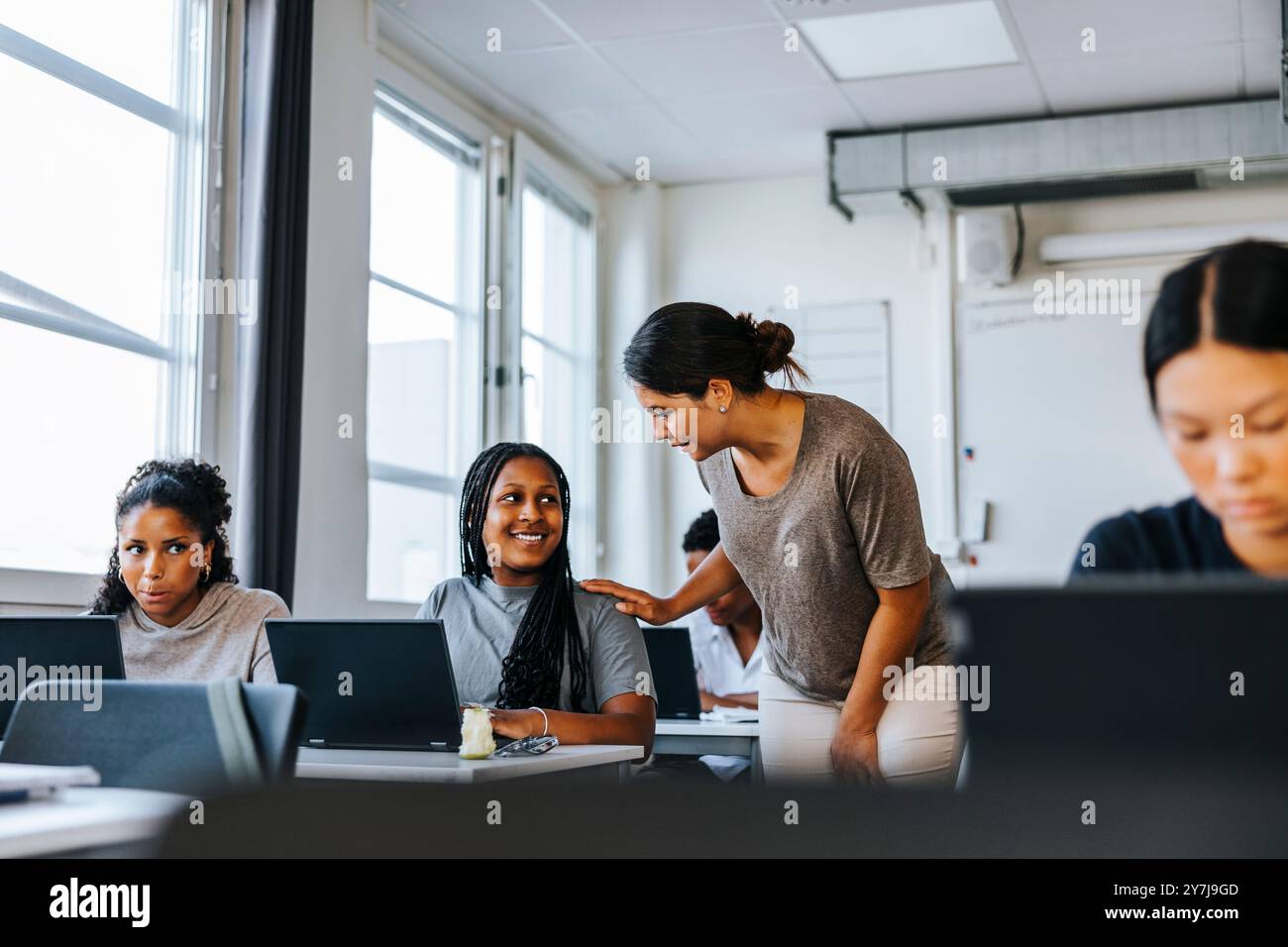 Enseignante aidant l'élève assis avec un ordinateur portable dans la salle de classe au collège Banque D'Images