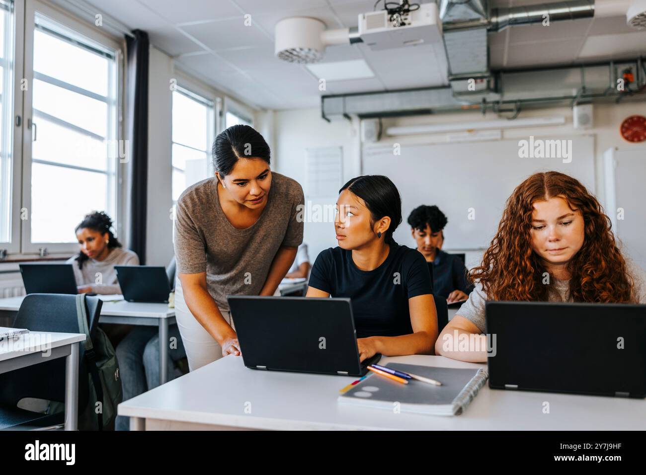 Professeur féminin aidant un adolescent assis avec un ordinateur portable dans une salle de classe au collège Banque D'Images
