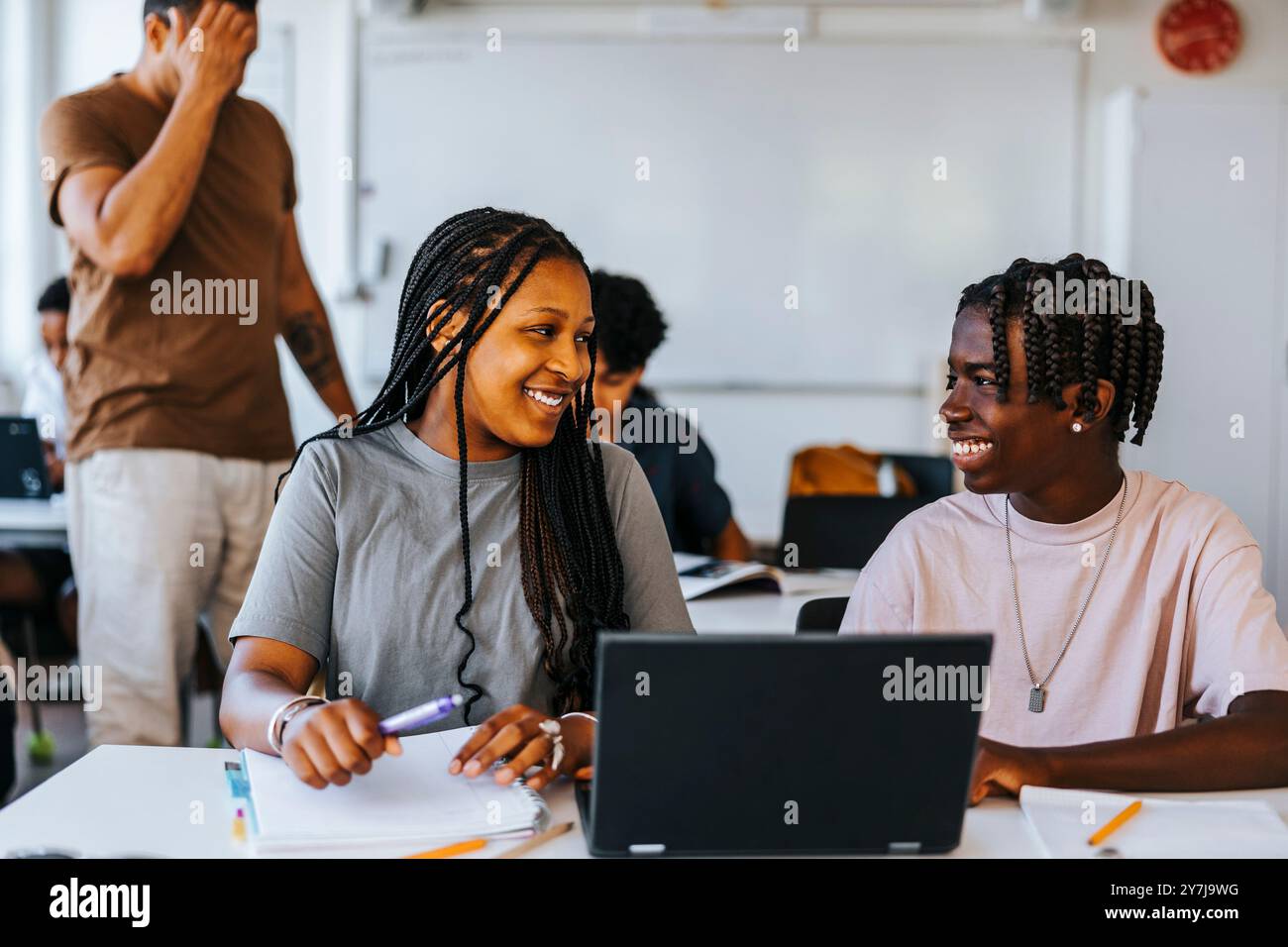 Heureux étudiants masculins et féminins étudiant ensemble tout en étant assis avec un ordinateur portable près du bureau dans la salle de classe à l'école Banque D'Images