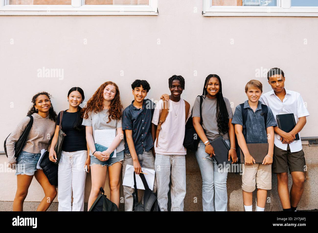 Portrait d'étudiants multiraciaux masculins et féminins du secondaire debout côte à côte près du mur du bâtiment de l'école Banque D'Images