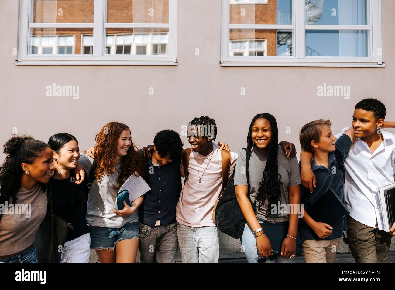 Étudiants multiraciaux de premier cycle, hommes et femmes, debout côte à côte près du mur du bâtiment de l'école Banque D'Images