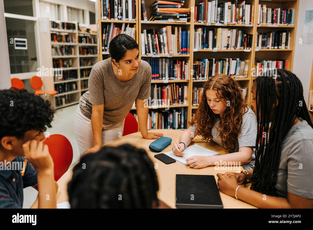 Bibliothécaire féminine aidant les élèves adolescents assis près de la table dans la bibliothèque à l'école Banque D'Images