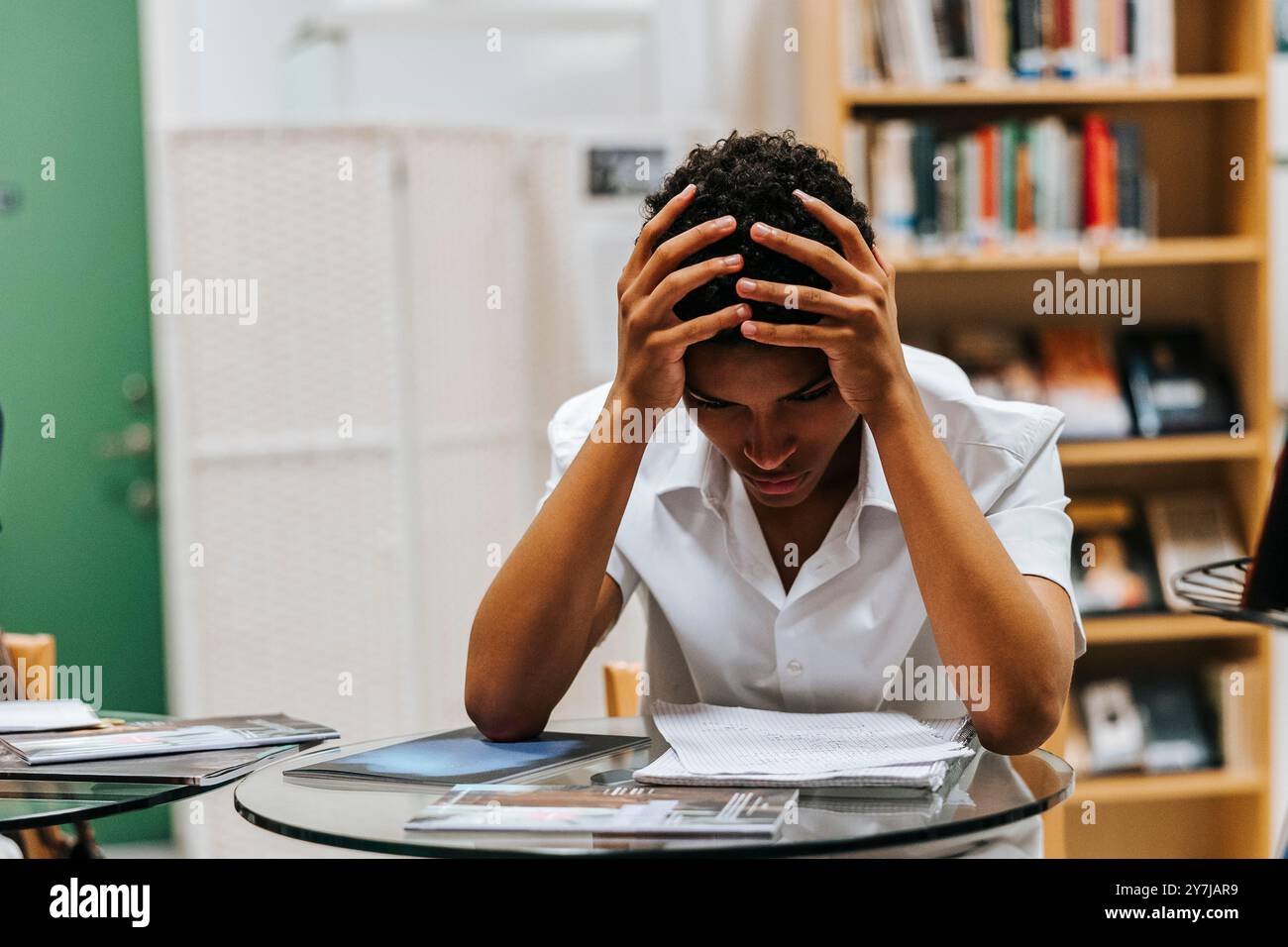 Adolescent inquiet assis la tête dans la main tout en étudiant à la bibliothèque de l'école Banque D'Images