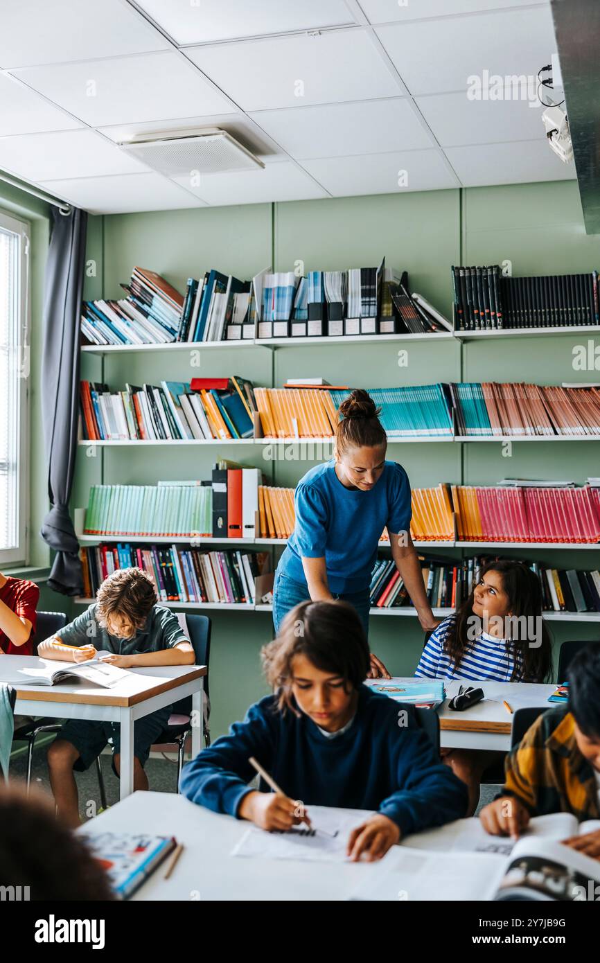 Enseignante aidant la fille pendant que les élèves étudient à la bibliothèque à l'école Banque D'Images