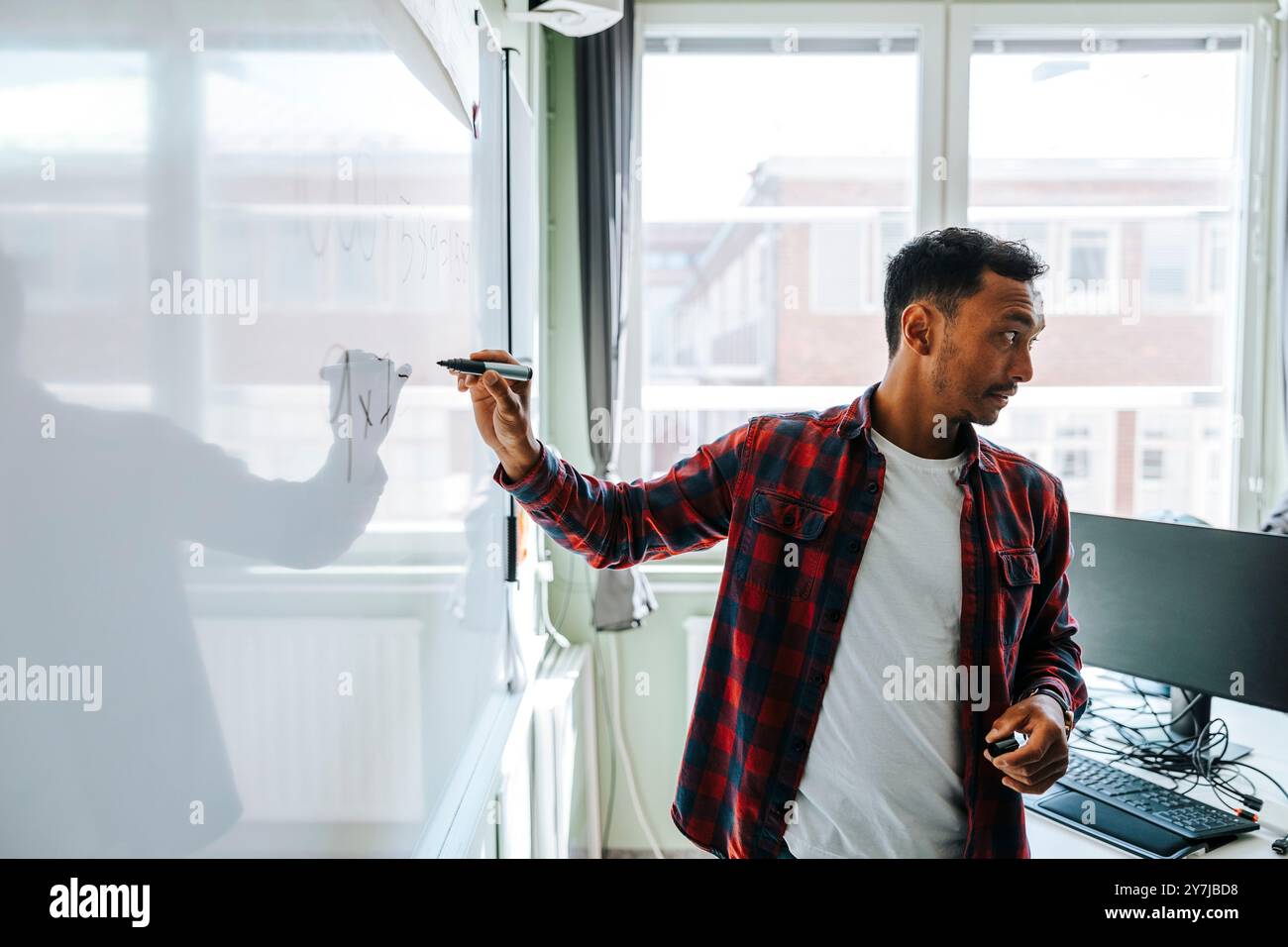 Professeur masculin tenant un stylo feutre tout en se tenant debout près du tableau blanc dans la salle de classe à l'école Banque D'Images