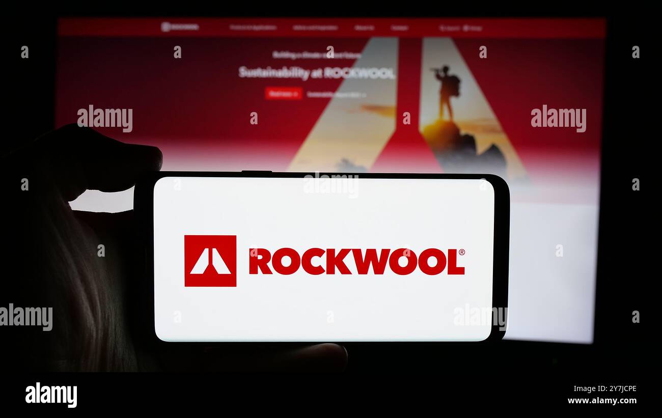Personne tenant le téléphone portable avec le logo de la société danoise de laine minérale Rockwool COMME sur l'écran en face de la page Web de l'entreprise. Concentrez-vous sur l'affichage du téléphone. Banque D'Images