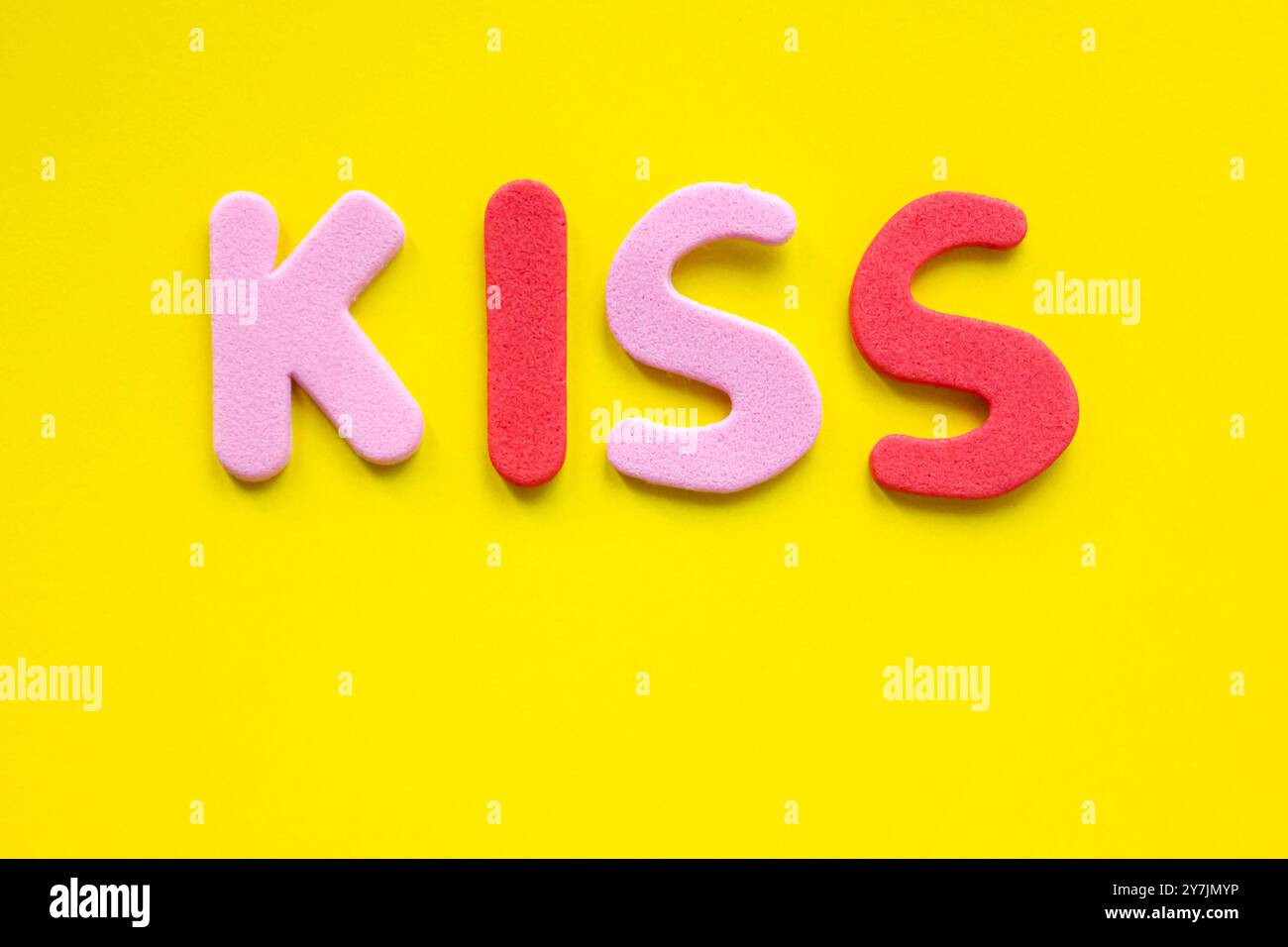 Le mot Kiss est composé de lettres rouges et roses de l'alphabet sur fond jaune avec espace. Vue de dessus, pose à plat. Banque D'Images