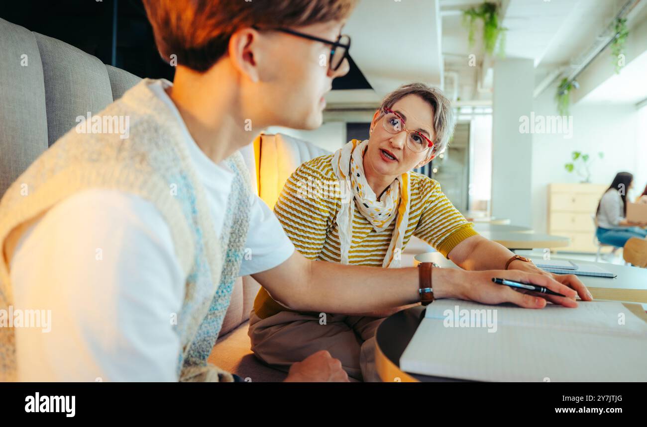 Un étudiant reçoit des conseils d'un conférencier dans une bibliothèque, reflétant le soutien éducatif, la collaboration et l'apprentissage ciblé. Banque D'Images
